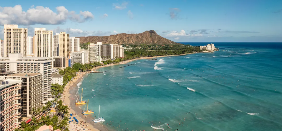 a beach with boats and buildings in the background with Diamond Head in the background